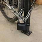 Black alarmed padlock securing a bicycle chain inside a covered bike store