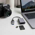 Grey SD and microSD card reader beside a camera and laptop