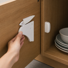 White hidden magnetic cabinet lock being positioned inside a wooden cupboard