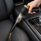 Cordless mini vacuum cleaning dry crumbs between a car seat and centre console